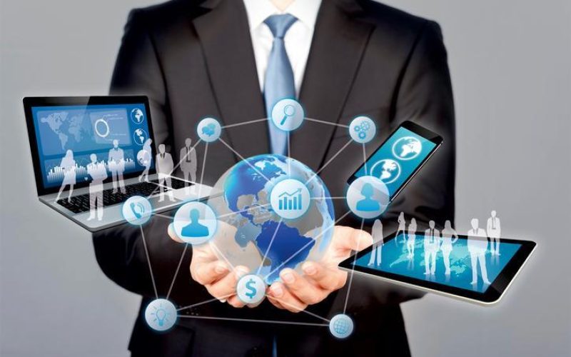 The image displays an individual dressed in a suit with several pieces of technology extending from his hands in a cloud formation.